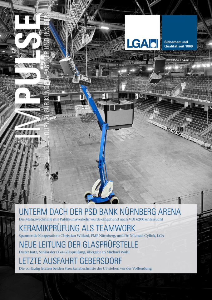 Das Bild zeigt das Cover eines Magazins mit dem Titel Impulse. Im Zentrum befindet sich eine große Veranstaltungshalle mit leeren Sitzreihen und einer offenen Fläche, über der ein blauer Hubsteiger unter dem Dach arbeitet. Die Konstruktion der Hallendecke und ein großer Videowürfel sind ebenfalls deutlich sichtbar.