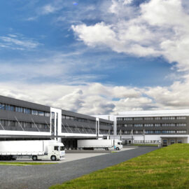 Grafisches Modell eines modernen Industriegebäudes mit mehreren Laderampen und geparkten weißen Lastwagen, im Vordergrund eine grasbewachsene Fläche mit einer telefonierenden Person.