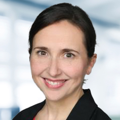 Dr. Marjolaine Pfaffinger trägt eine schwarze Jacke. Der Hintergrund ist unscharf und zeigt ein Büro.