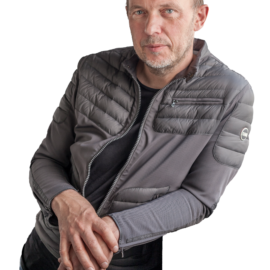 Das Bild zeigt eine Person mit einem grauen Jacke, das gesteppte Partien an Schultern und Oberarmen aufweist. Die Person steht lässig zur Seite gelehnt.