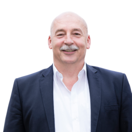 Das Bild zeigt eine Person in einem dunklen Sakko über einem weißen Hemd.