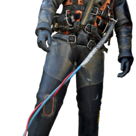 Das Bild zeigt eine Person in einem Tiefseetauchanzug mit Helm und Sichtfenster. Der Anzug ist mit mehreren Gurten, Schnallen und Schläuchen ausgestattet, die in Rot, Blau und Weiß gehalten sind. Die Person hält oder ist mit diesen Kabeln verbunden.