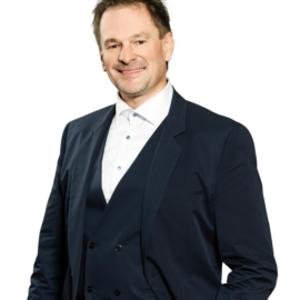 Das Bild zeigt eine Person in einem dunkelblauen Anzug mit weißem Hemd.