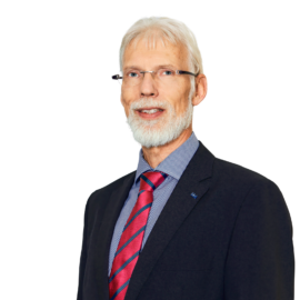 Das Bild zeigt eine Person in einem dunklen Sakko, einem hellblauen Hemd und einer rot gestreiften Krawatte.