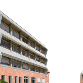 Zwei moderne Gebäude mit auffälliger Architektur stehen nebeneinander. Sie bestehen aus rötlich-braunen Ziegeln, haben mehrere Etagen und Fenster mit horizontalen Lamellen. Die kantigen Formen verleihen den Bauten ein markantes Erscheinungsbild.