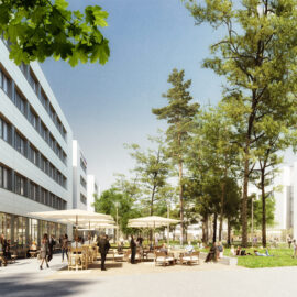Das Bild zeigt einen Außenbereich mit mehreren Tischen und Sonnenschirmen, an denen Menschen sitzen. Weitere Personen gehen durch die parkähnliche Umgebung mit Rasenflächen und hohen Bäumen. Im Hintergrund stehen moderne, mehrstöckige Gebäude mit großen Fenstern unter einem klaren, sonnigen Himmel.