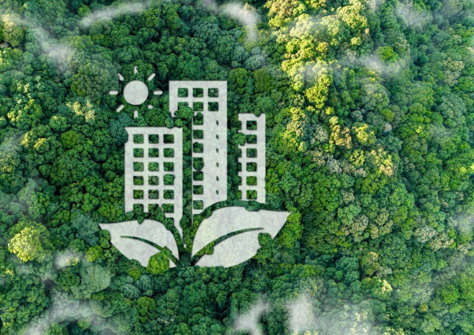 Das Bild zeigt eine Draufsicht auf einen dichten grünen Wald, in dem eine große grafische Darstellung integriert ist. Die Grafik besteht aus drei stilisierten Hochhäusern, die von zwei Blättern umrahmt werden, sowie einer Sonne über den Gebäuden. Die Gestaltung symbolisiert die Verbindung von urbanem Bauen mit Natur und Nachhaltigkeit.
