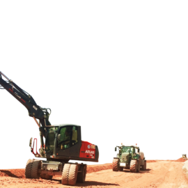 Das Bild zeigt eine Baustelle mit zwei schweren Baumaschinen, die auf einem unbefestigten Weg arbeiten. Im Vordergrund befindet sich ein Atlas-Bagger mit einem roten Anbaugerät, im Hintergrund ein grünes, traktorähnliches Fahrzeug.