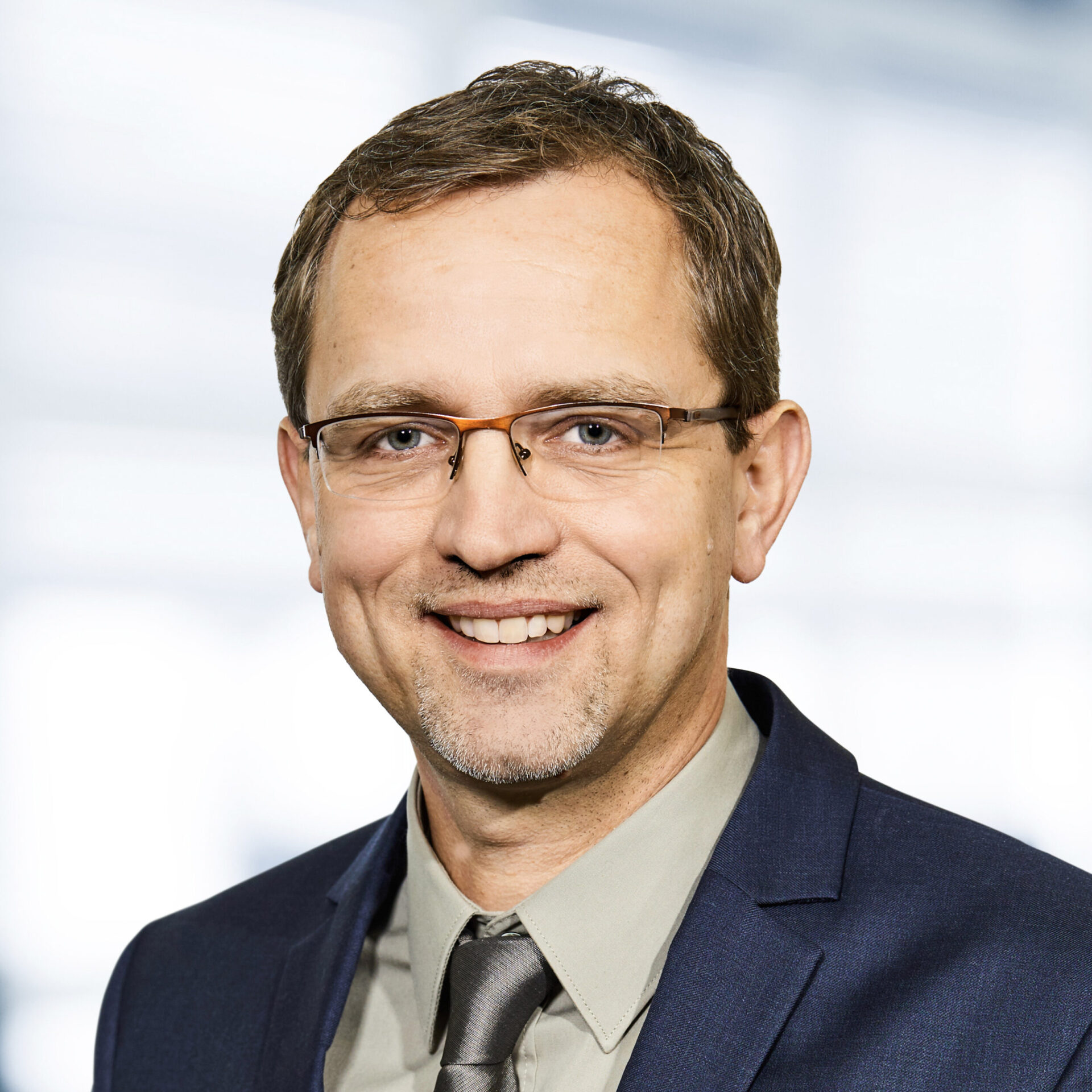 Ralph Bußler trägt einen Anzug mit Krawatte. Der Hintergrund ist unscharf und zeigt ein Büro.