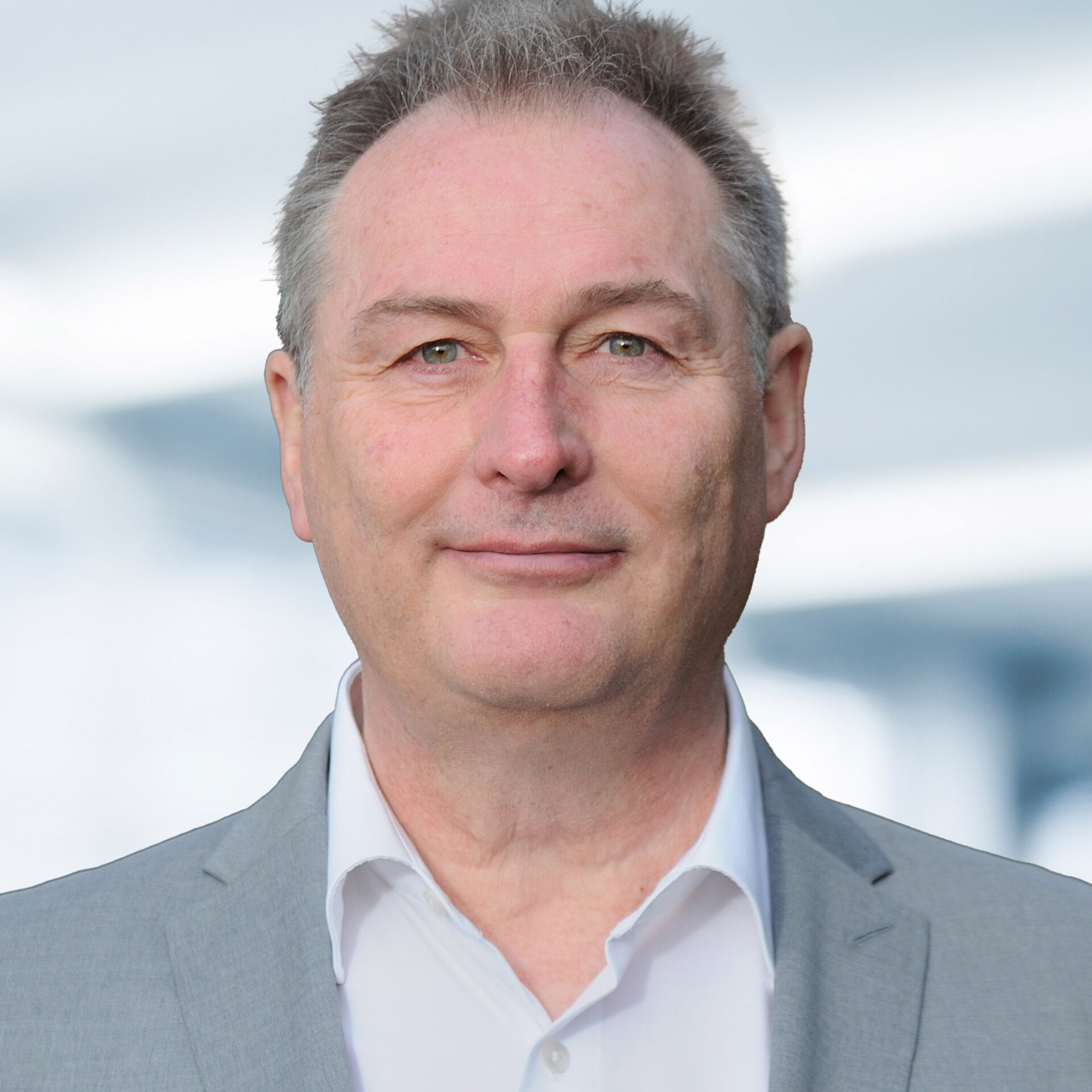 Sven Dotzauer trägt ein hellgraues Sakko und ein weißes Hemd. Der Hintergrund ist unscharf und zeigt ein Büro.