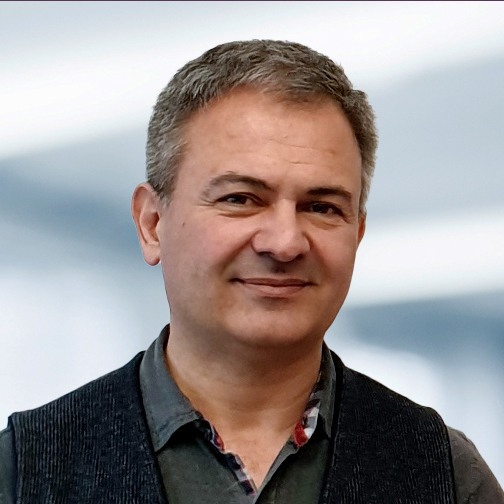 Stefan Eder trägt ein dunkel gefärbtes Hemd und eine schwarze Weste. Der Hintergrund ist unscharf und zeigt ein Büro.