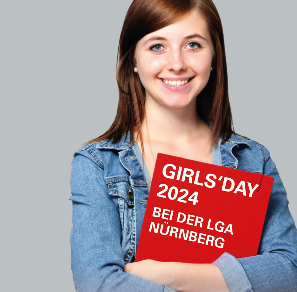 Eine Person mit braunen Haaren und Jeansjacke hält ein rotes Schild mit der Aufschrift „GIRLS'DAY 2024 BEI DER LGA NÜRNBERG“.