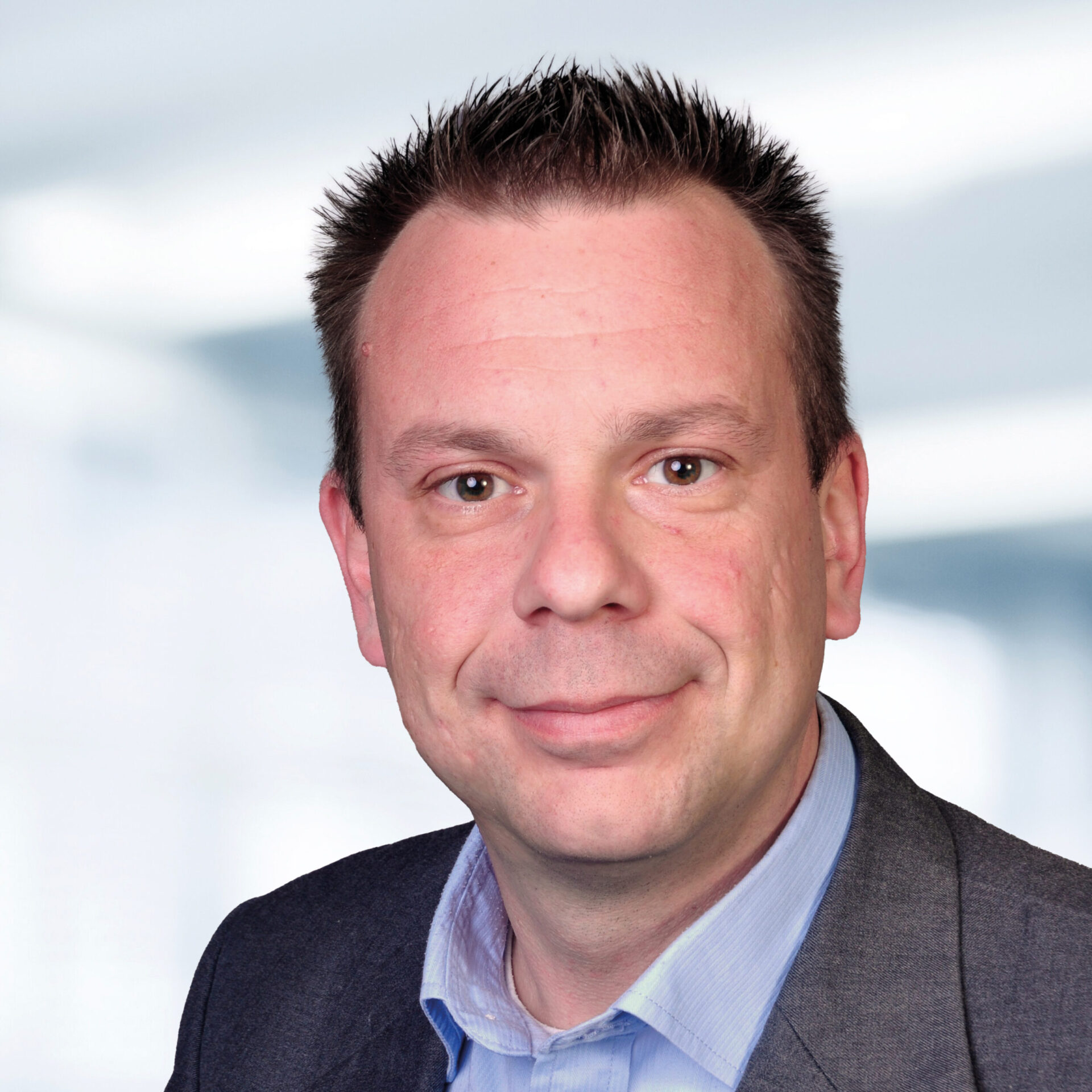 Nico Hartlep trägt ein Sakko und ein hellblaues Hemd. Der Hintergrund ist unscharf und zeigt ein Büro.