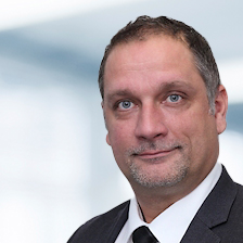 Sven Homburg trägt einen Anzug mit Krawatte. Der Hintergrund ist unscharf und zeigt ein Büro.