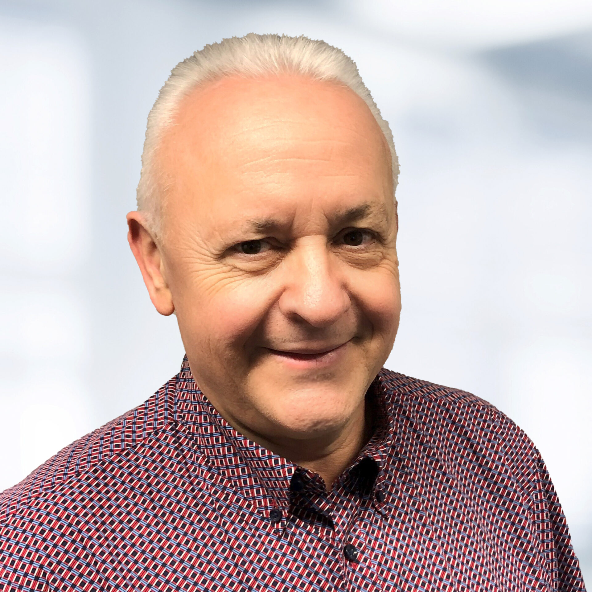 Georg Hubatschek trägt ein rot-blau gemustertes Hemd. Der Hintergrund ist unscharf und zeigt ein Büro.