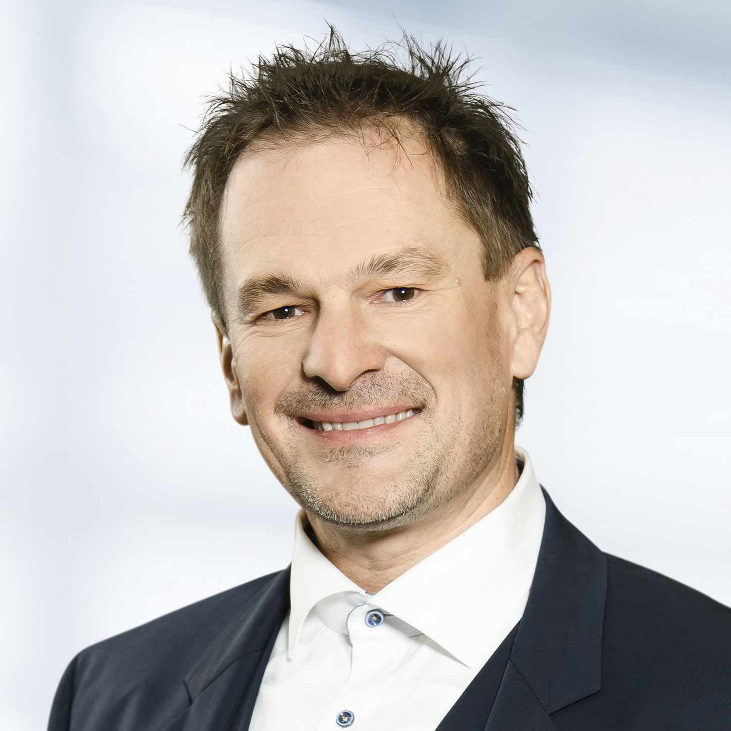 Alexander Krauß trägt ein dunkles Sakko über einem weißen Hemd. Der Hintergrund ist unscharf und zeigt ein Büro.