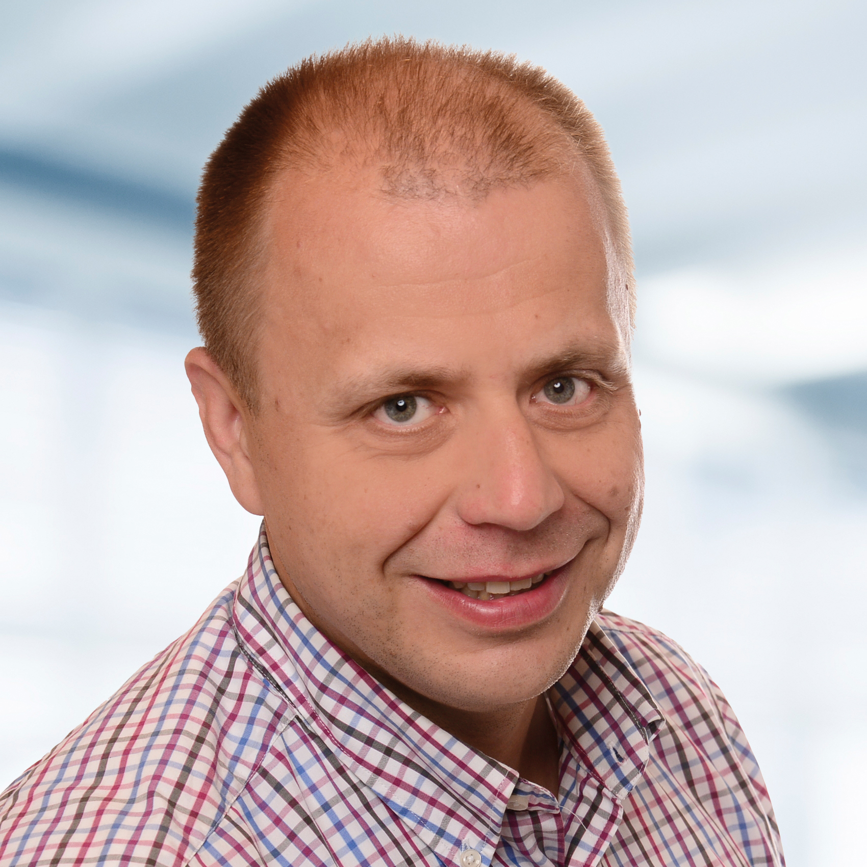 Dr. Ingo Kurzhöfer trägt ein kariertes Hemd. Der Hintergrund ist unscharf und zeigt ein Büro.