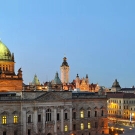 Panoramaaufnahme von Leipzig bei Dämmerung mit dem Bundesverwaltungsgericht im Vordergrund, erkennbar an seiner großen Kuppel und klassizistischen Architektur, im Hintergrund historische Gebäude und moderne Bauten wie das City-Hochhaus Leipzig.