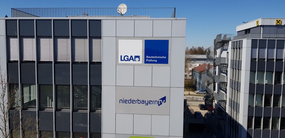 Außenansicht eines modernen Gebäudes mit den Beschriftungen „LGA Bautechnische Prüfung“ und „niederbayernTV“, sowie weiteren Gebäuden im Hintergrund.