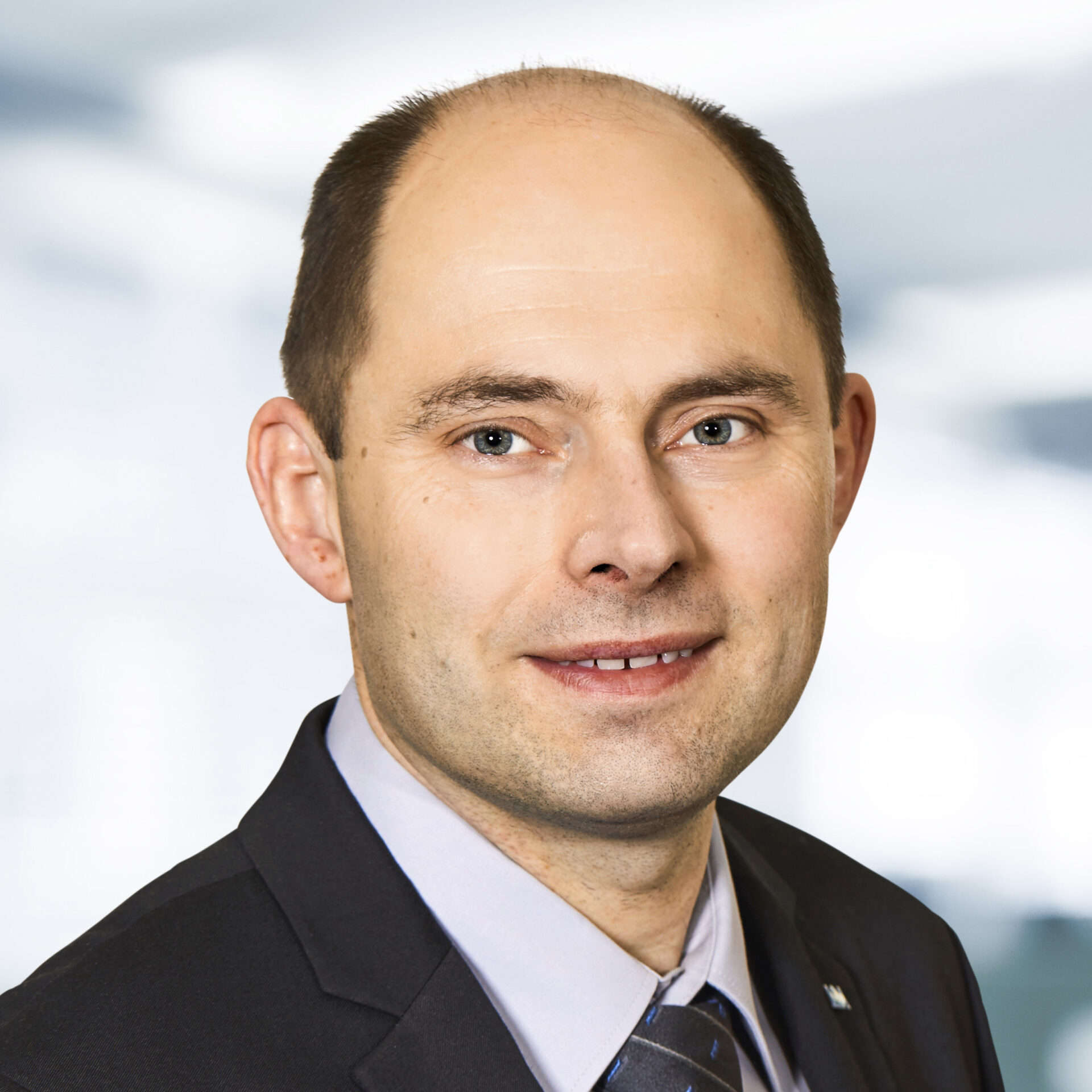 Christian Liebl trägt einen Anzug und eine Krawatte. Der Hintergrund ist unscharf und zeigt ein Büro.
