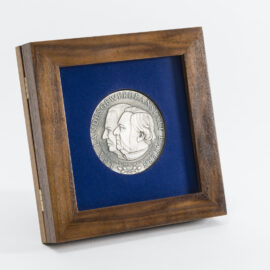 Gerahmte silberne Medaille mit zwei geprägten Profilen vor blauem Hintergrund, eingefasst in einem Holzrahmen, mit der Inschrift „LGA LANDESGEWERBEANSTALT BAYERN“.