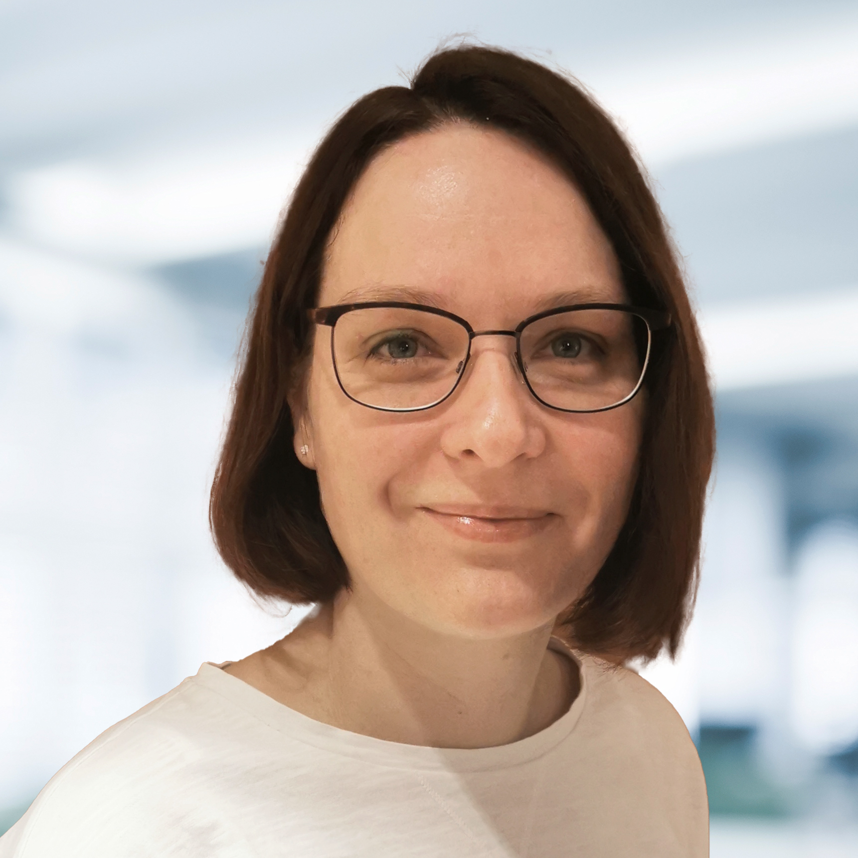 Marin Mende trägt ein weißes Oberteil. Der Hintergrund ist unscharf und zeigt ein Büro.