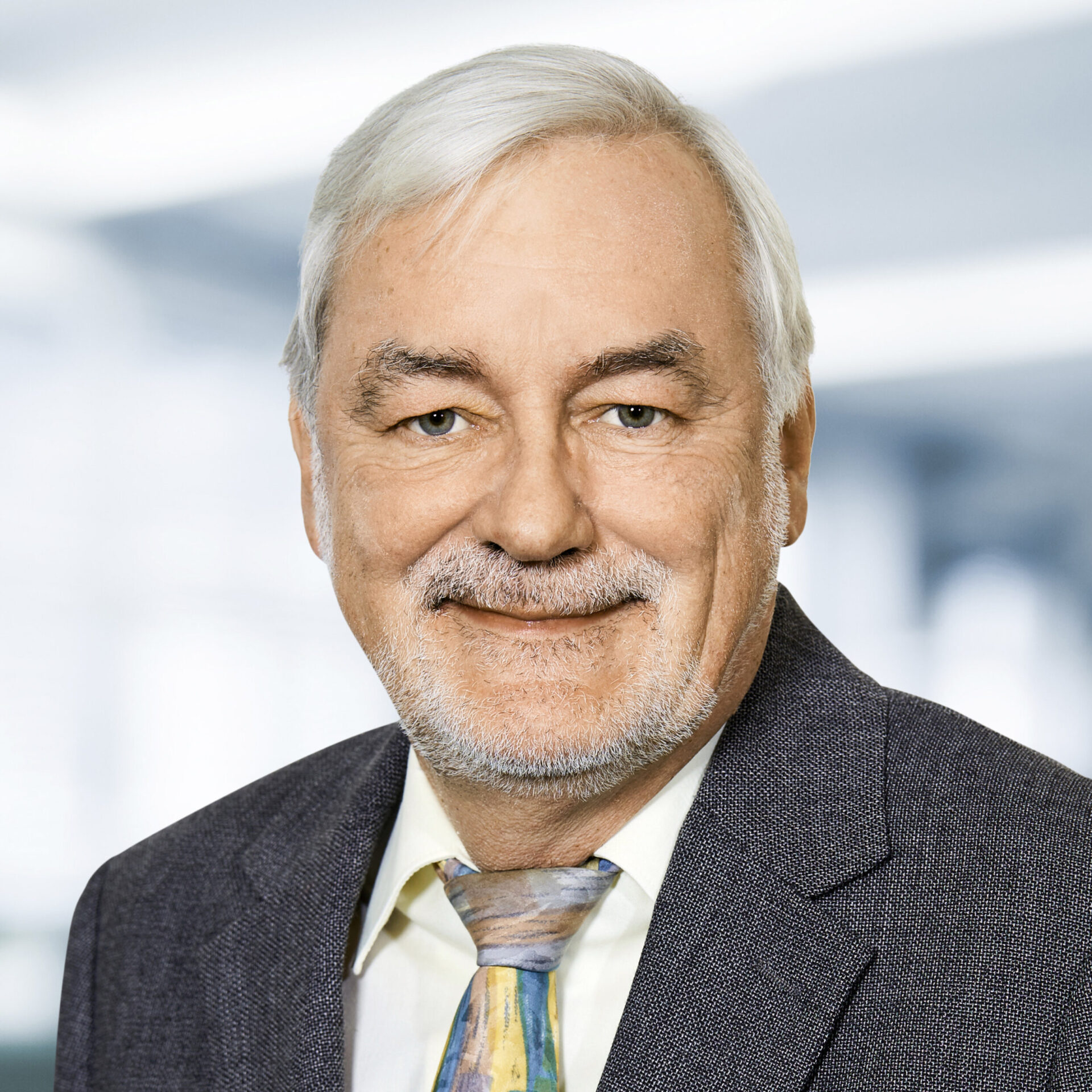 Dr. Bernd Müllner trägt ein Sakko, ein Hemd und eine Krawatte. Der Hintergrund ist unscharf und zeigt ein Büro.