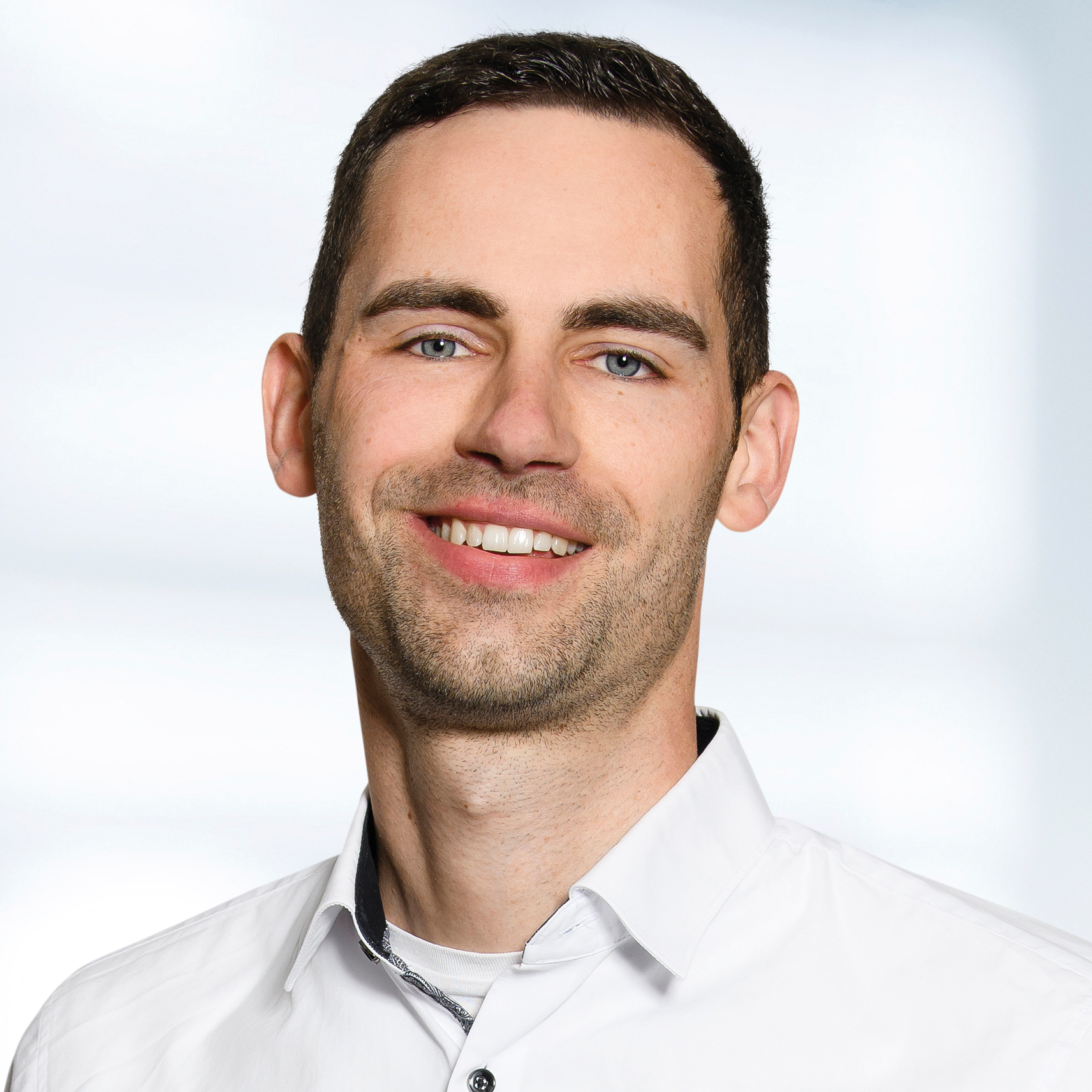 Dr. Jürgen Schreiner trägt ein weißes Hemd mit Kragen. Der Hintergrund ist unscharf und zeigt ein Büro.