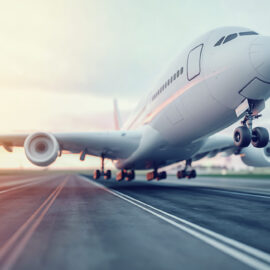 Ein großes Verkehrsflugzeug hebt von einer Asphaltpiste ab. Das vordere Fahrwerk ist bereits in der Luft, während das hintere noch den Boden berührt. Im Hintergrund ist ein klarer Himmel mit einigen Wolken zu sehen, beleuchtet von Sonnenlicht von der linken Seite.
